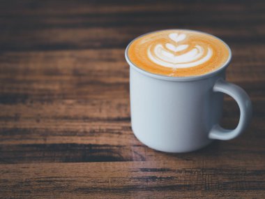 Kahverengi ahşap masada gri seramik bardak şeklinde sanat kalbi şekilli sıcak latte kahve.. 