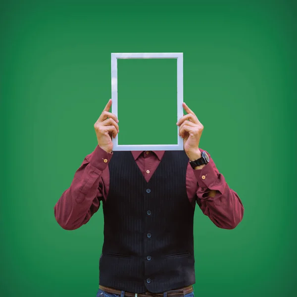 A man holds a picture frame at the level of his head. Isolate. Green background.