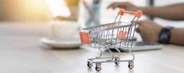 shopping cart on table with hand of people on laptop background 
