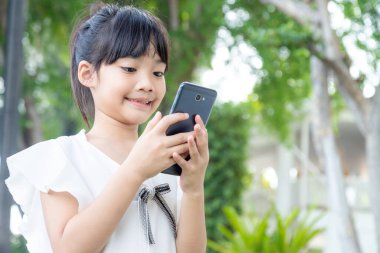 Akıllı telefon kullanan café'de küçük Asya kız. Doğal ışık açık hava yaşam tarzı.