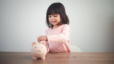Tatlı Asyalı kız gelecek için para biriktirmek adına kumbaraya para koyuyor.