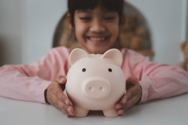 Küçük Asyalı kız domuz kumbarasında para biriktiriyor, tasarruf yapmayı öğreniyor, çocuk gelecek eğitim için para biriktiriyor. Para, finans, sigorta ve insan konsepti