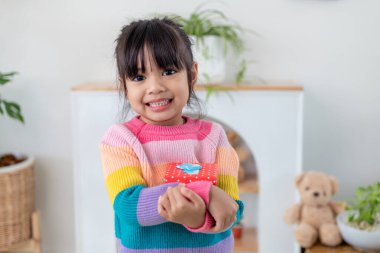 Küçük Asyalı kız gülümsüyor ve oturma odasında kırmızı hediye kutusunu tutuyor. Noel 'de ve yeni yılda hediye kutusunu tutan çocuk..