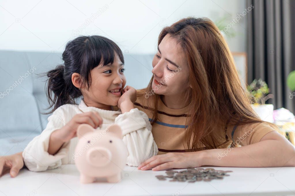 Mother and daughter putting coins into piggy bank. Family budget and savings concept. Junior Savings Account concept