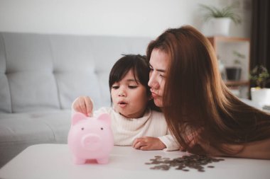 Anne ve kızı kumbaraya bozuk para koyuyor. Aile bütçesi ve tasarruf konsepti. Küçük Tasarruf Hesabı kavramı