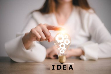 hand touching on light bulb on wood block with Word Idea, new idea concept with innovation and inspiration, innovative technology in science and communication concept.
