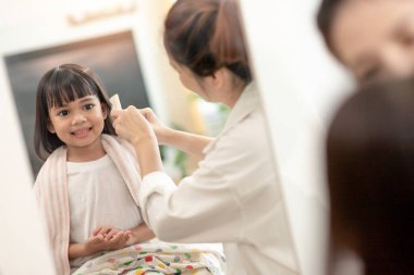 Asyalı anne evde, evinde, Covid-19 Coronavirus 'tan korunurken kızına saç kesiyor. Kişisel karantina ve sosyal uzaklık kavramı.