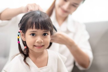 Genç Asyalı anne kızının saçını bağlıyor.