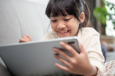 İnternette tablet kullanan küçük bir kız kanepede oturan ya da arkadaşıyla internetten konuşan bir çocuk, sabah oturma odasında dinlenen çocuk, yeni teknoloji konsepti olan çocuklar.