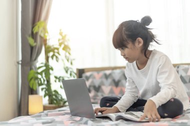 Küçük Asyalı kız yatakta yatarken dizüstü bilgisayar kullanıyor.