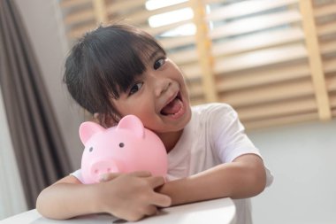 Küçük Asyalı kız domuz kumbarasında para biriktiriyor, tasarruf yapmayı öğreniyor, çocuk gelecek eğitim için para biriktiriyor. Para, finans, sigorta ve insan konsepti