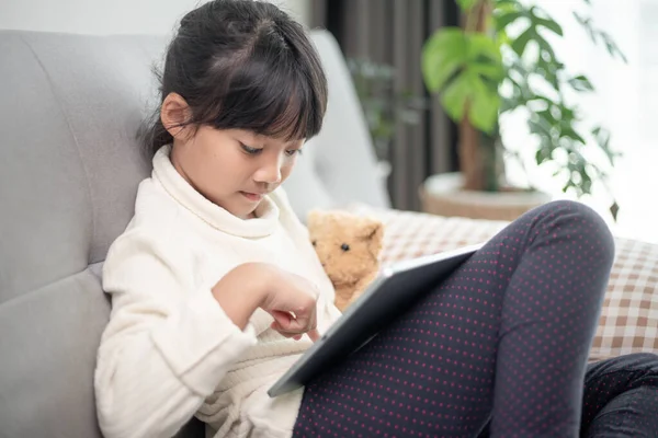 İnternette tablet kullanan küçük bir kız kanepede oturan ya da arkadaşıyla internetten konuşan bir çocuk, sabah oturma odasında dinlenen çocuk, yeni teknoloji konsepti olan çocuklar.
