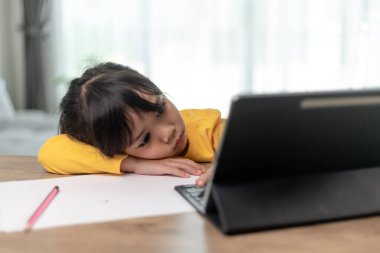 Küçük Asyalı kız tek başına oturuyor ve canı sıkkın bir yüzle dışarı bakıyor, okul öncesi çocuğu ödevlerinden sıkılmış, şımarık çocukla baş aşağı masaya uzanıyor.