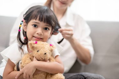 Genç Asyalı anne kızının saçını bağlıyor.