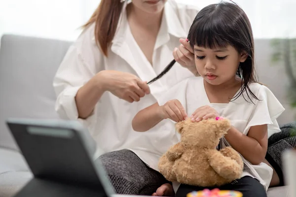 Genç Asyalı anne kızının saçını bağlıyor.