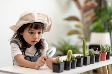 Çocuk nazikçe kaktüsün yeni gövdesine dokunuyor. Bir elinde büyüteç, bir elinde büyüteç tutuyor. Doğa eğitimi, Montessori ve gözlem becerileri konsepti..