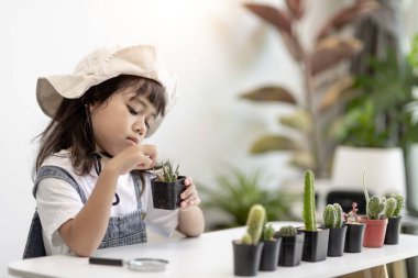 Çocuk nazikçe kaktüsün yeni gövdesine dokunuyor. Bir elinde büyüteç, bir elinde büyüteç tutuyor. Doğa eğitimi, Montessori ve gözlem becerileri konsepti..