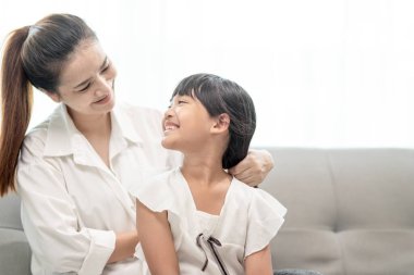 Genç Asyalı anne kızının saçını bağlıyor.