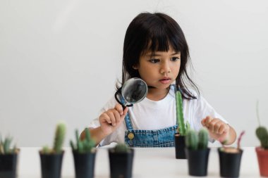 Çocuk nazikçe kaktüsün yeni gövdesine dokunuyor. Bir elinde büyüteç, bir elinde büyüteç tutuyor. Doğa eğitimi, Montessori ve gözlem becerileri konsepti..