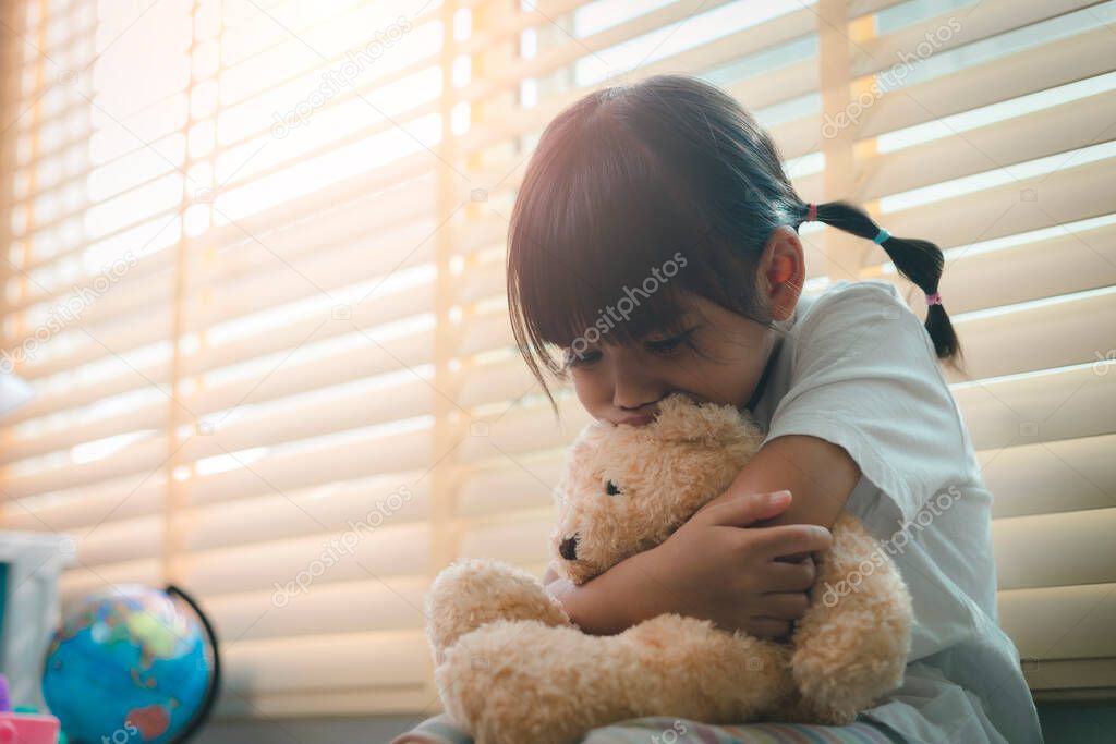 Close up lonely little girl hugging toy, sitting at home alone, upset unhappy child waiting for parents, thinking about problems, bad relationship in family, psychological trauma