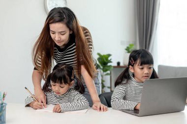 Asyalı küçük kız evde annesiyle online ders alıyor. Anaokulu çocuğu dizüstü bilgisayar kullanır ev ödevi yapar, okul öğretmeninden dijital uzaktan internete geçer ve annesinden destek alır..