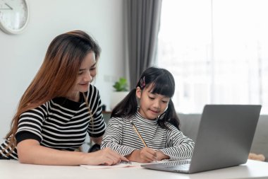 Asyalı küçük kız evde annesiyle online ders alıyor. Anaokulu çocuğu dizüstü bilgisayar kullanır ev ödevi yapar, okul öğretmeninden dijital uzaktan internete geçer ve annesinden destek alır..