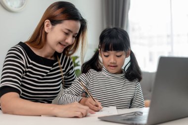 Asyalı küçük kız evde annesiyle online ders alıyor. Anaokulu çocuğu dizüstü bilgisayar kullanır ev ödevi yapar, okul öğretmeninden dijital uzaktan internete geçer ve annesinden destek alır..