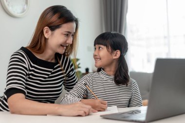 Asyalı küçük kız evde annesiyle online ders alıyor. Anaokulu çocuğu dizüstü bilgisayar kullanır ev ödevi yapar, okul öğretmeninden dijital uzaktan internete geçer ve annesinden destek alır..