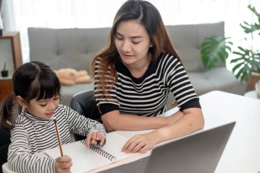Asyalı küçük kız evde annesiyle online ders alıyor. Anaokulu çocuğu dizüstü bilgisayar kullanır ev ödevi yapar, okul öğretmeninden dijital uzaktan internete geçer ve annesinden destek alır..