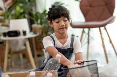 Gülümseyen çocuklar plastik şişeleri ve kağıdı bir çöp kutusuna koyarken eğleniyorlar.