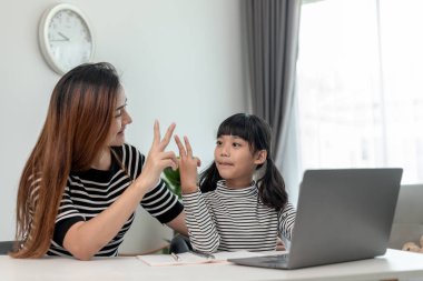 Asyalı küçük kız evde annesiyle online ders alıyor. Anaokulu çocuğu dizüstü bilgisayar kullanır ev ödevi yapar, okul öğretmeninden dijital uzaktan internete geçer ve annesinden destek alır..