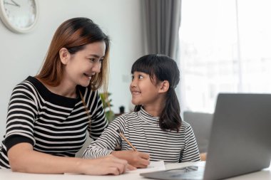 Asyalı küçük kız evde annesiyle online ders alıyor. Anaokulu çocuğu dizüstü bilgisayar kullanır ev ödevi yapar, okul öğretmeninden dijital uzaktan internete geçer ve annesinden destek alır..