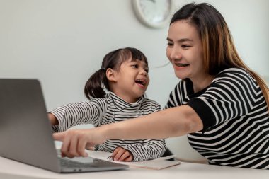 Asyalı küçük kız evde annesiyle online ders alıyor. Anaokulu çocuğu dizüstü bilgisayar kullanır ev ödevi yapar, okul öğretmeninden dijital uzaktan internete geçer ve annesinden destek alır..