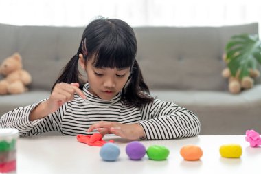 Küçük kız iyi aydınlatılmış bir odada renkli oyun hamuru kullanmayı öğreniyor. 