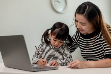 Asyalı küçük kız evde annesiyle online ders alıyor. Anaokulu çocuğu dizüstü bilgisayar kullanır ev ödevi yapar, okul öğretmeninden dijital uzaktan internete geçer ve annesinden destek alır..