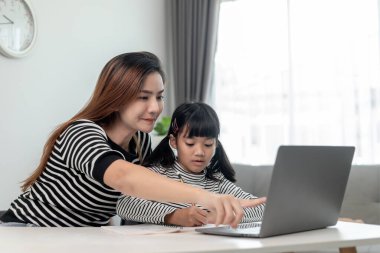 Asyalı küçük kız evde annesiyle online ders alıyor. Anaokulu çocuğu dizüstü bilgisayar kullanır ev ödevi yapar, okul öğretmeninden dijital uzaktan internete geçer ve annesinden destek alır..