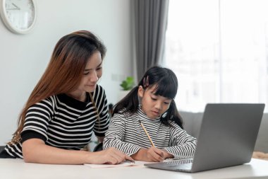 Asyalı küçük kız evde annesiyle online ders alıyor. Anaokulu çocuğu dizüstü bilgisayar kullanır ev ödevi yapar, okul öğretmeninden dijital uzaktan internete geçer ve annesinden destek alır..