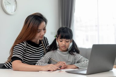 Asyalı küçük kız evde annesiyle online ders alıyor. Anaokulu çocuğu dizüstü bilgisayar kullanır ev ödevi yapar, okul öğretmeninden dijital uzaktan internete geçer ve annesinden destek alır..