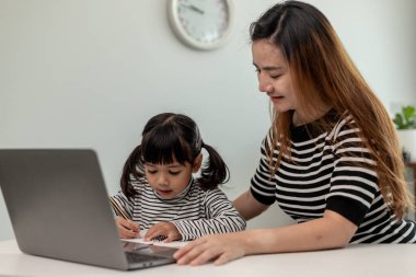 Asyalı küçük kız evde annesiyle online ders alıyor. Anaokulu çocuğu dizüstü bilgisayar kullanır ev ödevi yapar, okul öğretmeninden dijital uzaktan internete geçer ve annesinden destek alır..