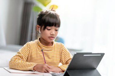 Online öğrenim sınıfındaki Asyalı kız öğrenciler evde Tablet ile çevrimiçi öğrenim görüyorlar.