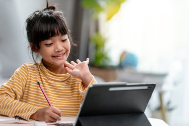 Online öğrenim sınıfındaki Asyalı kız öğrenciler evde Tablet ile çevrimiçi öğrenim görüyorlar.