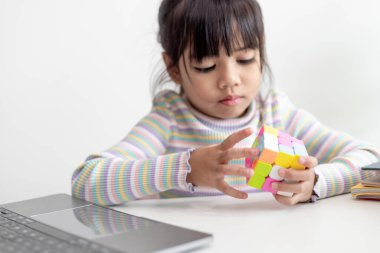 NAKHON RATCHASIMA, THAILAND - JULY 14, 2022:Asian little cute girl holding Rubik's cube in her hands. Rubik's cube is a game that increases the intelligence of children.