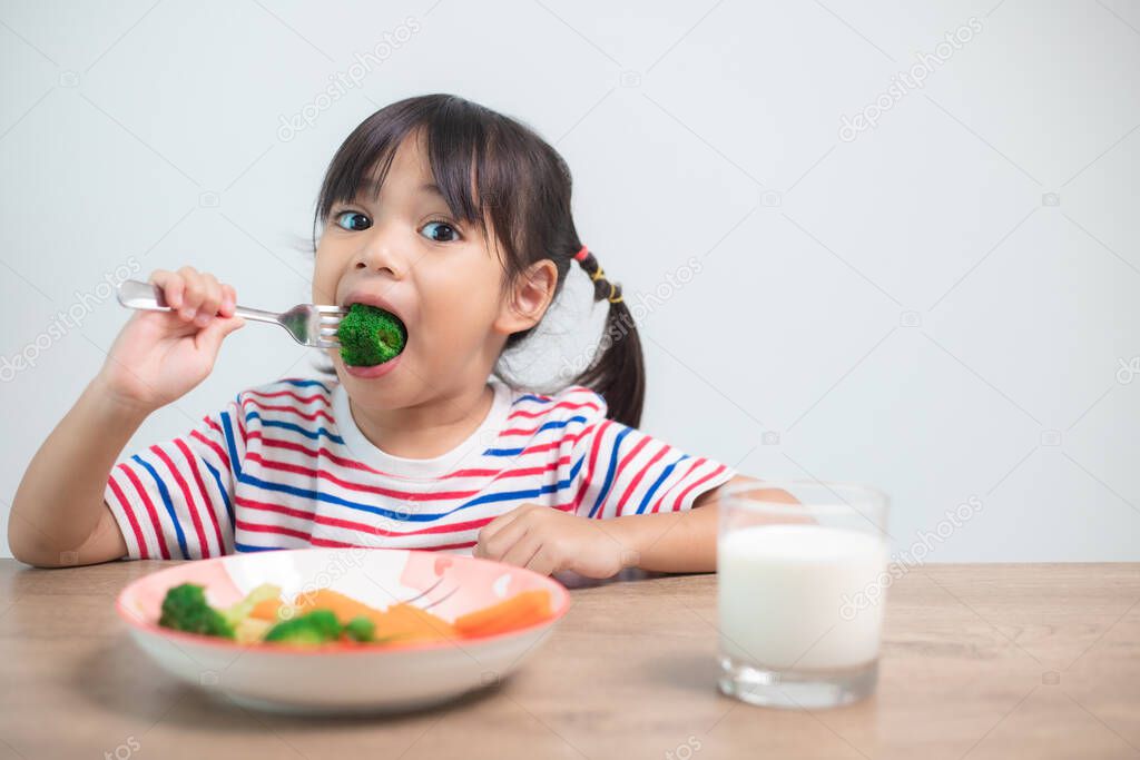 Cute asian child girl eating healthy vegetables and milk for her meal