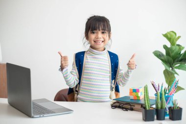Sırt çantalı Asyalı ilkokul öğrencisi kız başparmağını kaldırıyor. Özgürlüğü kutlayan mutlu Asyalı çocuk öğrenci. Okul Konseptine geri dön.