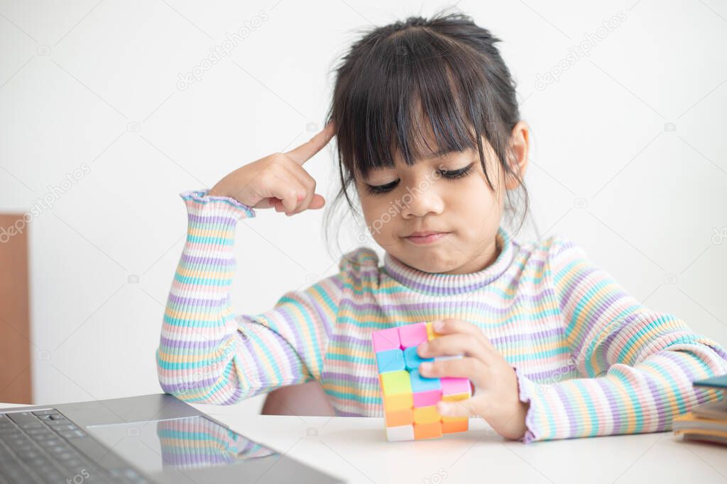 NAKHON RATCHASIMA, THAILAND - JULY 14, 2022:Asian little cute girl holding Rubik's cube in her hands. Rubik's cube is a game that increases the intelligence of children.