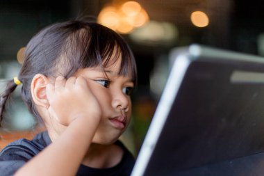 Happy Asian Child girl looks at tablet on the table