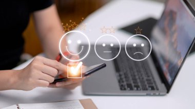 Müşteri hizmetleri değerlendirme konsepti. Akıllı telefon kullanmak, sanal ekranda gülümseyen yüz ifadelerine basmaktır..