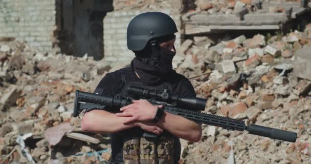 Український солдат з гвинтівкою стоїть навпроти зруйнованого будинку і оглядається навколо.. — стокове відео
