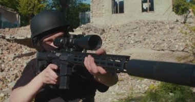 Bir asker keskin nişancı tüfeğiyle yıkılmış bir evin arka planına ateş ediyor..