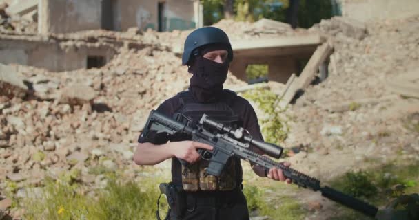 A soldier with a rifle stands against the backdrop of a house destroyed by the war. — Stockvideo